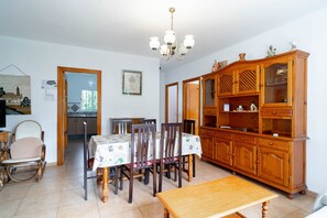 A dining area with a wooden table and chairs, a kitchen in the background, and a wooden cabinet with glass doors.