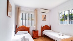 Une chambre d’hôtel avec deux lits simples, une table de chevet en bois, une petite table et une fenêtre avec des barreaux.