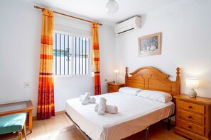 Une chambre d’hôtel comprenant un lit, une table de chevet avec une lampe, une fenêtre avec des rideaux et un appareil de climatisation.