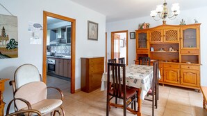 Un coin repas avec une table dressée pour quatre personnes, un buffet en bois doté de portes en verre, et une cuisine visible à travers une porte ouverte.