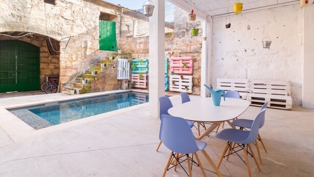 A poolside area with a stone wall, a green door, and a white table with blue chairs.