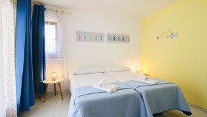 A hotel room with two beds, a small table with a lamp, and a wall with house-shaped decorations.