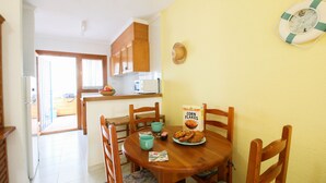 A dining area with a wooden table, chairs, a bowl of fruit, a box of corn flakes, and a life preserver on the wall.