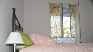 Et soveværelse med en seng, en lampe og et vindue med blomstrede gardiner.