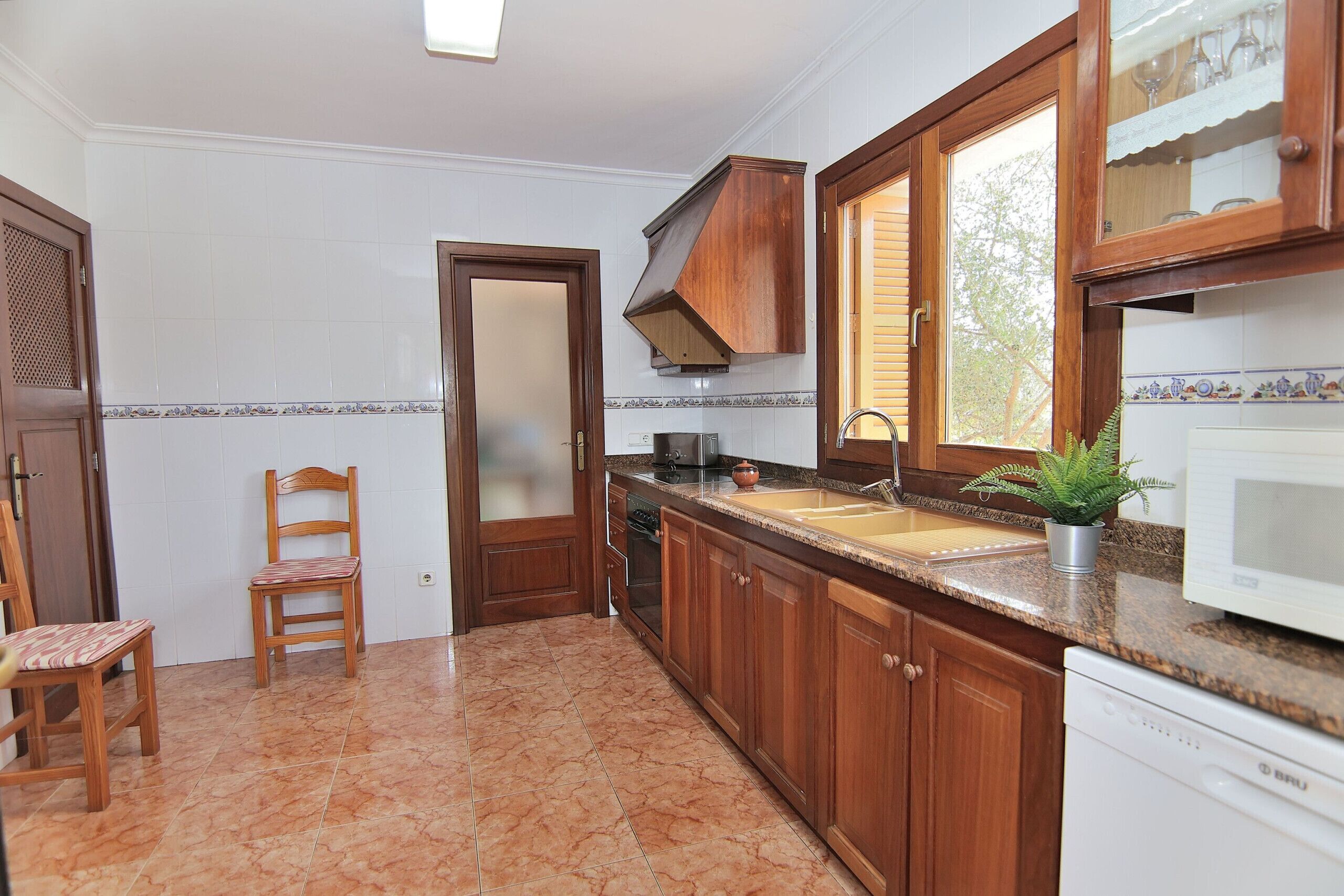 A kitchen with wooden cabinets, a granite countertop, a built-in oven, a microwave, and a window with blinds.