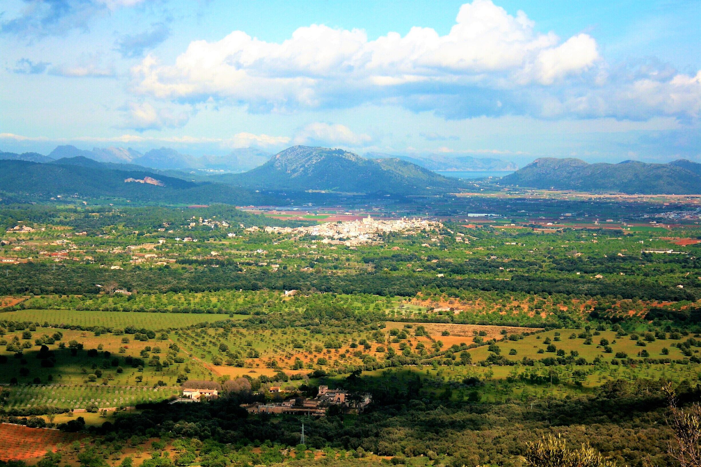 Vista panorámica de un valle con edificios dispersos, una montaña destacada al fondo y un pequeño grupo de construcciones en primer plano.