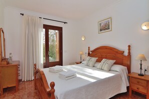 A neatly arranged bedroom with a wooden bed, a nightstand with a lamp, a dresser, and a window with curtains.