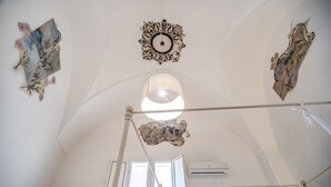 Un plafond haut orné de motifs décoratifs, un luminaire central et un appareil de climatisation.