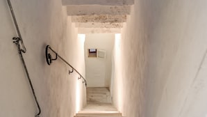 Un escalier étroit et mal éclairé, doté d’une rambarde métallique et d’une petite fenêtre en haut.