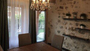 Un comedor con una mesa de madera, sillas, una araña y paredes de piedra.