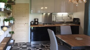 Una cocina compacta con electrodomésticos modernos, un comedor con mesa y sillas de madera, y plantas decorativas en estantes.