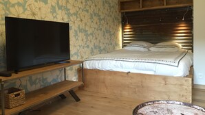 Un dormitorio con estructura de cama de madera, un televisor sobre un mueble de madera y un papel tapiz floral.