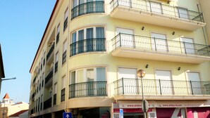 A multi-story building with balconies, a visible storefront with signage, and a clear sky.