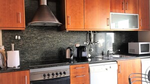 A kitchen with wooden cabinets, a stainless steel range hood, a microwave, a kettle, and a dishwasher.