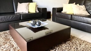 A modern living room with two black leather sofas, a glass coffee table with decorative items, and a shaggy rug.