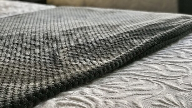 A bed with a textured grey blanket and a patterned duvet.