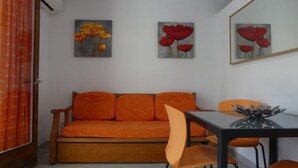 A room with a sofa, a dining table, and chairs. There are paintings on the wall. - Alexis Plus  Zeus Salou 9011 (Salou)