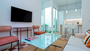 A modern living room with a glass coffee table, red upholstered chairs, a flat-screen TV mounted on the wall, and a kitchen area with bar stools and a countertop. - Genteel Home Galera Terrace II (Seville)