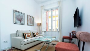 A modern living room with a glass coffee table, a sofa with cushions, a red chair, a TV mounted on the wall, and a window with curtains. - Genteel Home Galera Terrace II (Seville)