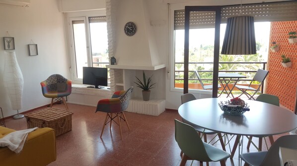 Un soggiorno con televisore, un tavolo da pranzo con sedie, un divano e una finestra vista all'esterno.
