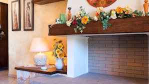 A fireplace with a brick surround, a wooden mantel decorated with flowers and a vase of sunflowers, and a table with a lamp and a candle. - Villa Rose - Marina Di Mancaversa (Marina di mancaversa)