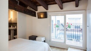 A bedroom with a bed, a small bedside table, a nightstand, a window with a view of a balcony, and a wooden ceiling. - Singular Stays A. San Vicente II (Valencia / València)