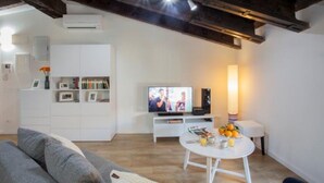 A modern living room with a white entertainment unit, a flat-screen TV, a round white table with books and a lamp, and a grey sofa. - Singular Stays A. San Vicente II (Valencia / València)