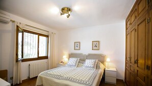 Ein Schlafzimmer mit einem großen Bett, zwei Nachttischen mit Lampen, einem Fenster mit Vorhängen und einem Holzschrank.