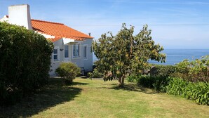 Une maison avec un toit recouvert de tuiles rouges, une façade blanche et une vue sur la mer.