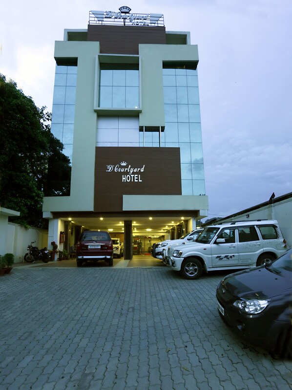 Un hotel con fachada moderna, un cartel que dice "D'Courtyard HOTEL" y varios vehículos estacionados frente a él.
