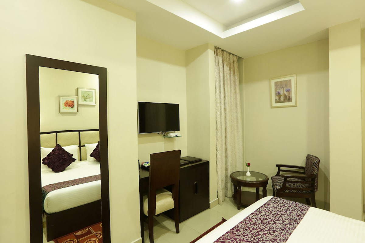 Habitación de hotel con cama, escritorio, silla, televisor y una mesita con un florero.
