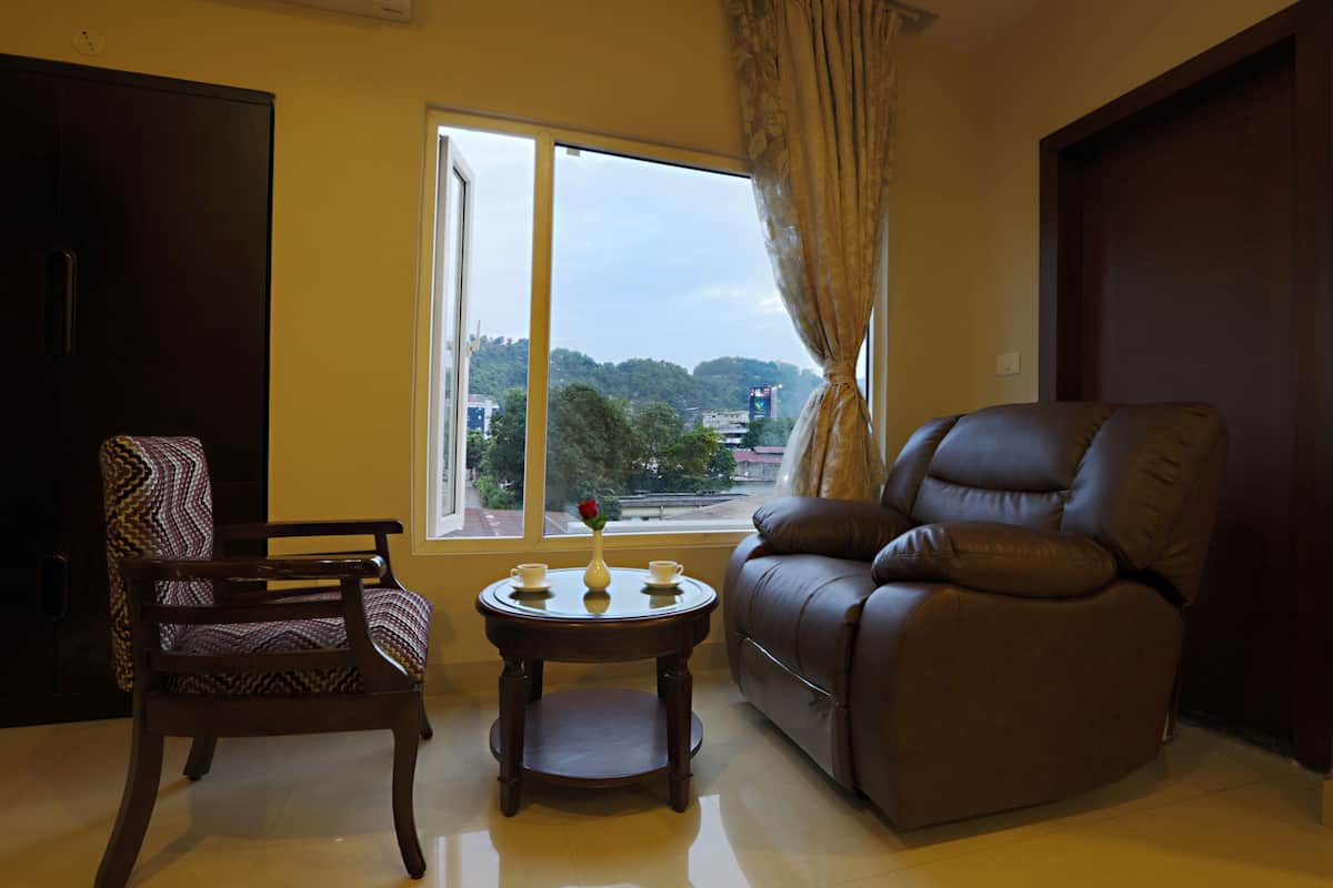 A living room with a sofa, a chair, a small table with a vase, and a window with a view of a cityscape.