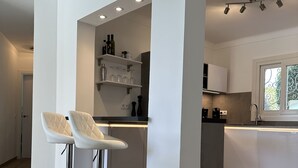 Uma cozinha moderna com armários brancos, uma ilha central e dois bancos.