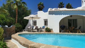 Uma área de piscina com um prédio branco, cadeiras de lounge e um espaço coberto para relaxar.