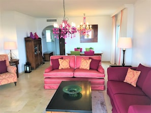 Een woonkamer met een roze bank, een groene salontafel en een kroonluchter.