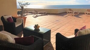 Eine Terrasse mit Korbmöbeln, einem kleinen Tisch und Blick aufs Meer.
