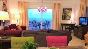 Ein Hotelzimmer mit Balkon, einer Couch, einem Esstisch, einem Fernseher und einem Kronleuchter.