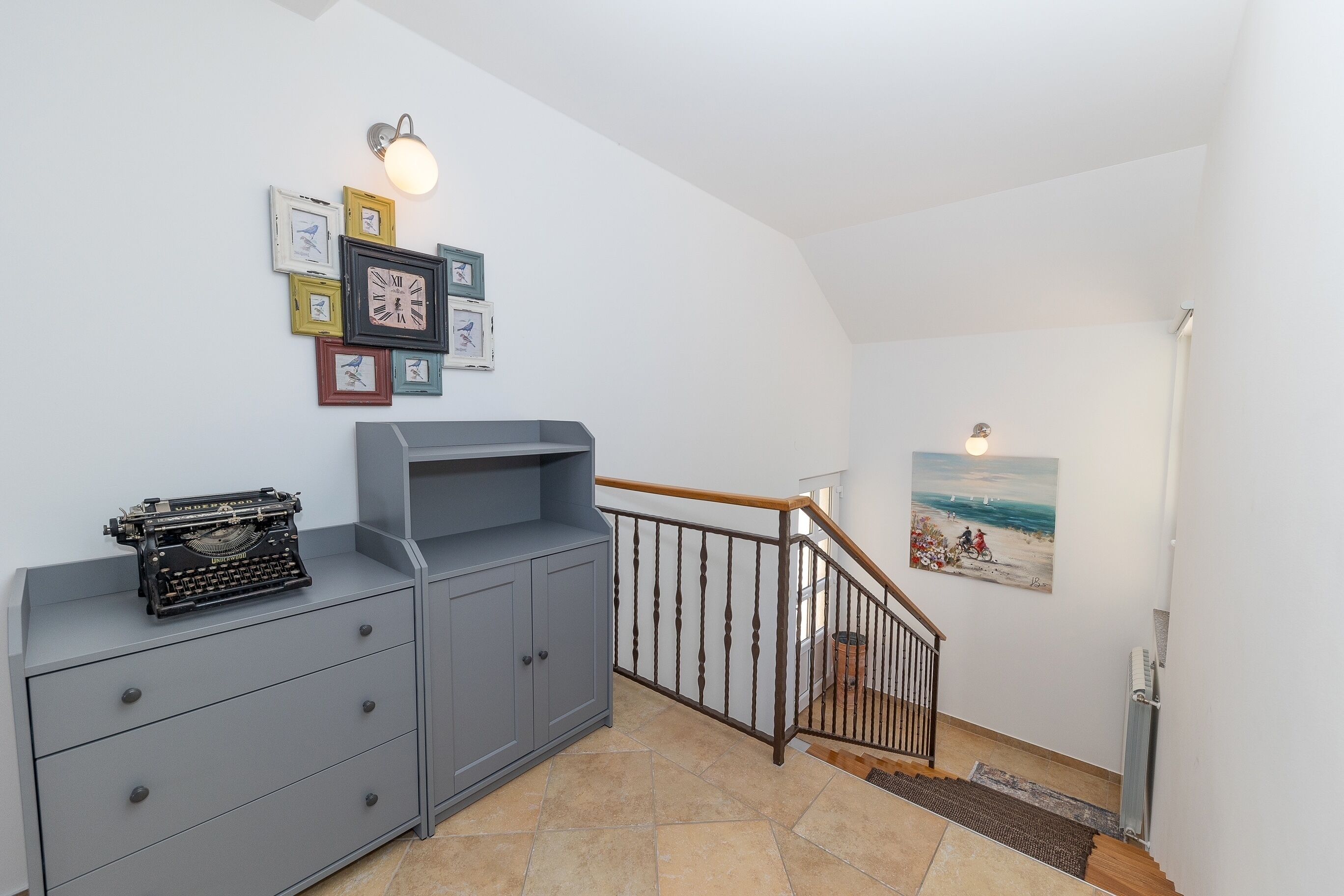 Een trap met een houten leuning en een zwarte balustrade, die leidt naar een kamer met een bureau en een vintage typmachine.