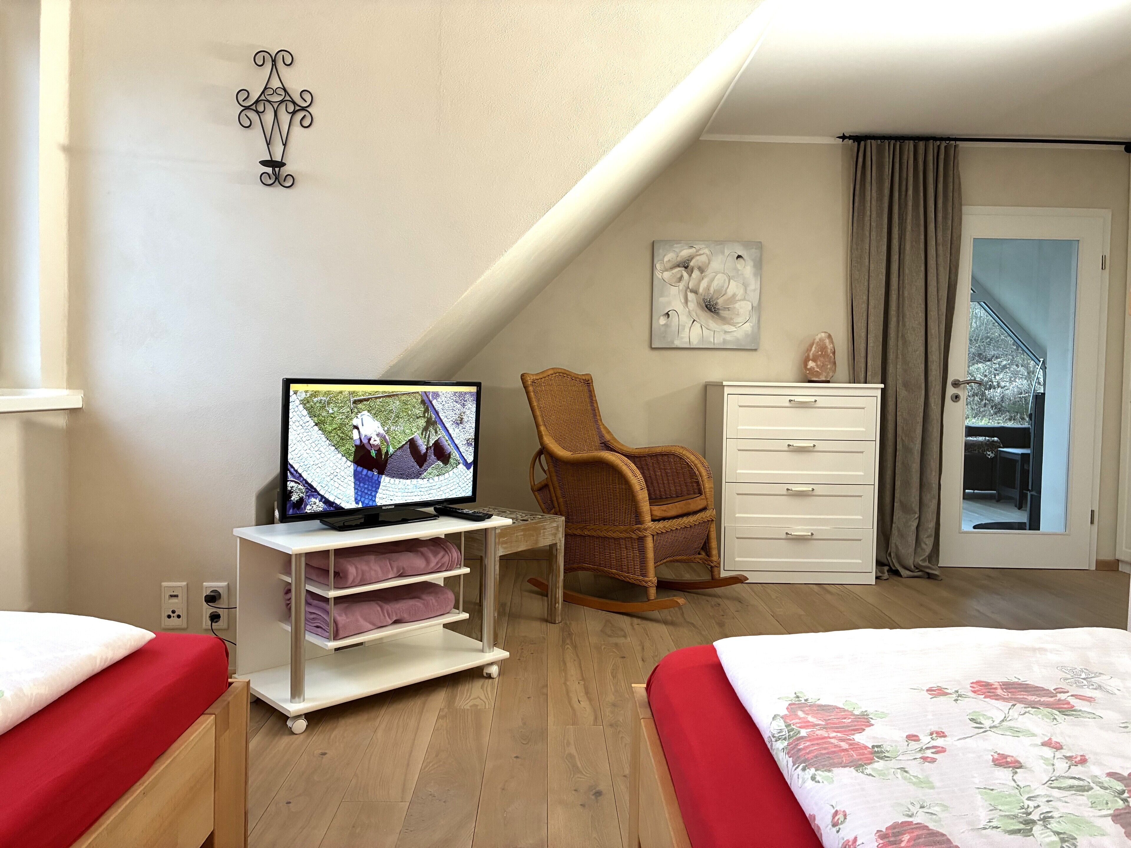 A bedroom with a TV, two beds, a chair, a dresser, and a painting.