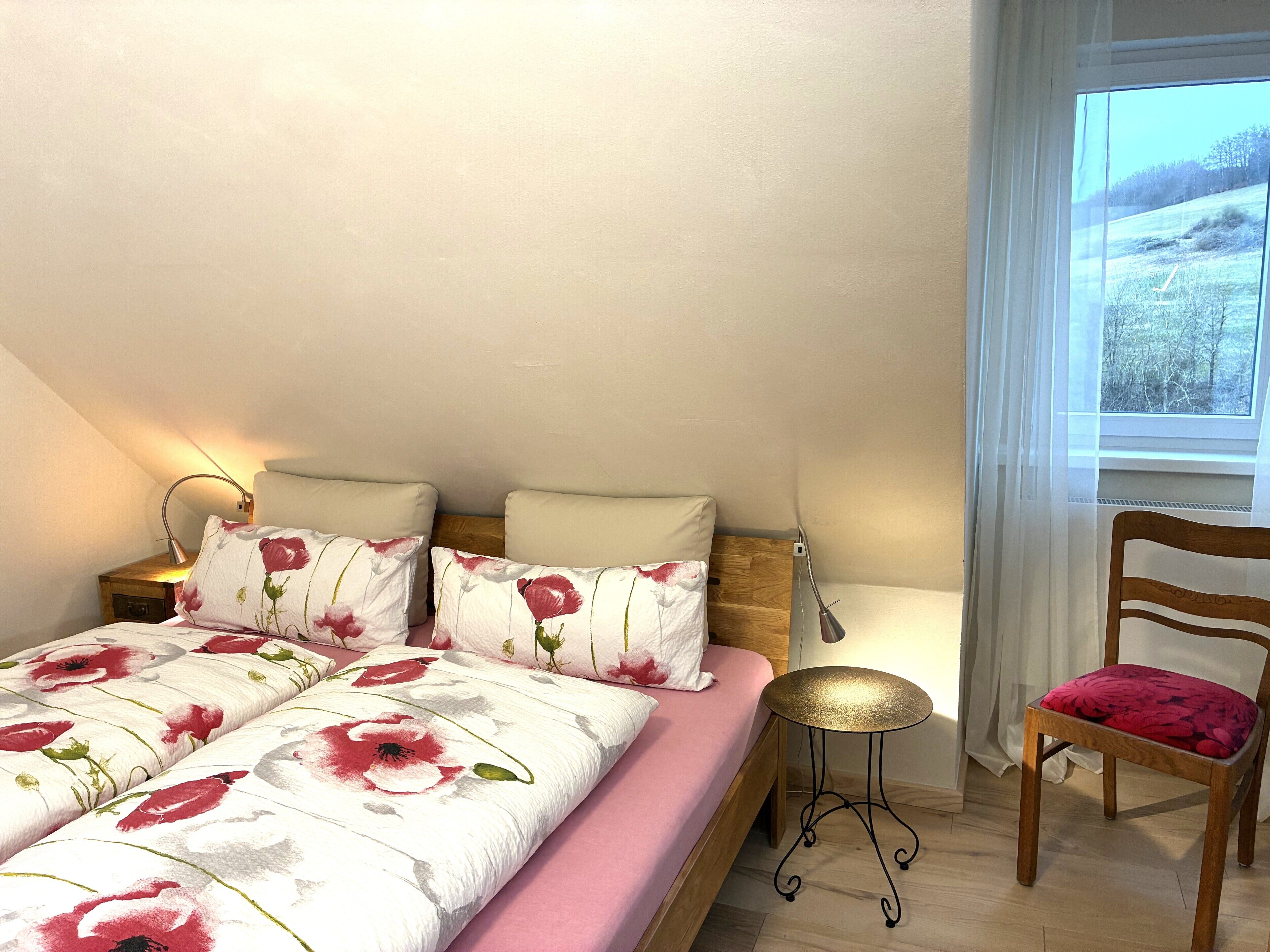 A bedroom with a bed, bedside tables, a chair, and a window with a view of a snowy landscape.