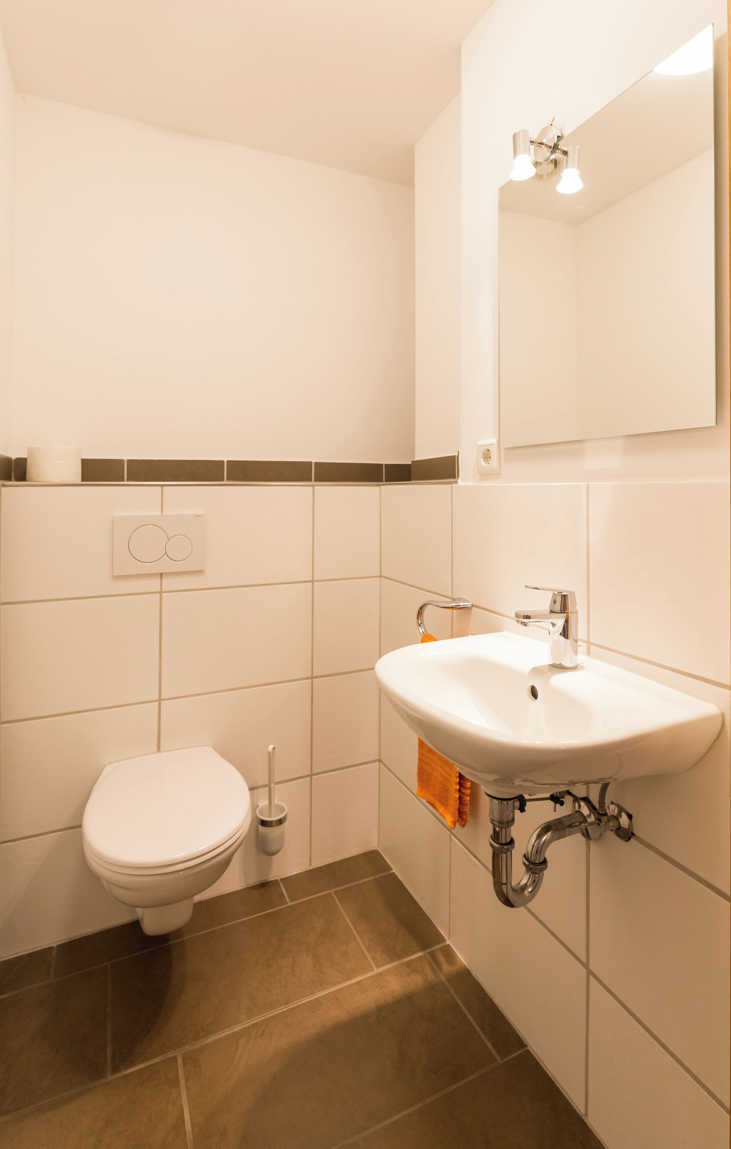 A bathroom with a white toilet, a sink with a mirror above it, and a wall-mounted light fixture.