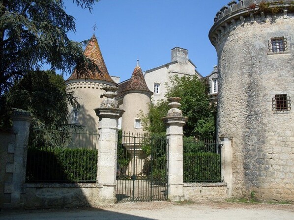 A historic stone castle with multiple towers, a gated entrance, and a well-maintained garden.