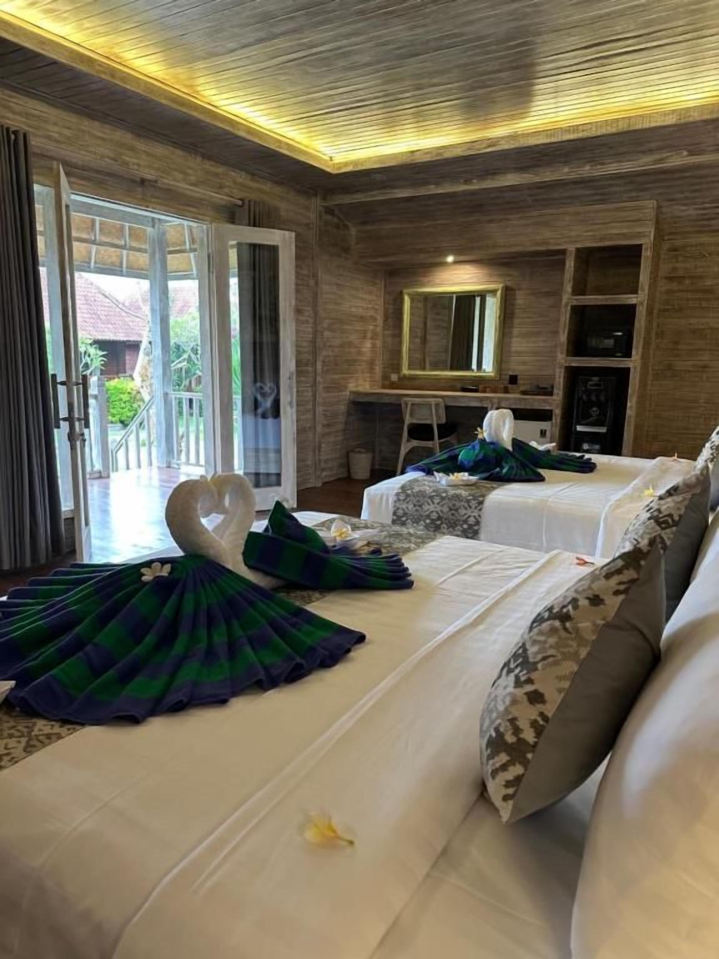 Une chambre d’hôtel avec un plafond en bois, un lit recouvert d’une couverture verte et bleue, un oreiller blanc et une petite table avec un miroir.