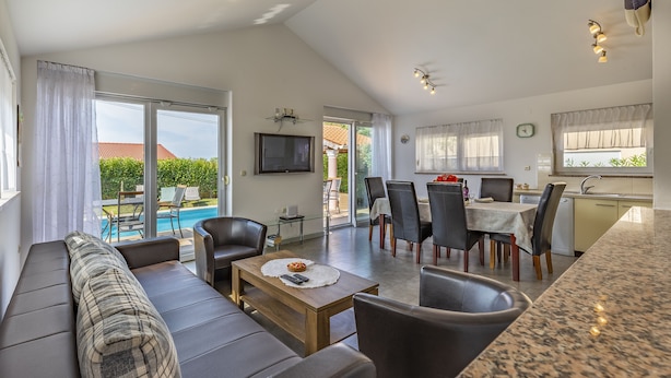 A spacious living area with a sofa, dining table, and chairs, a kitchen with a sink, and a pool visible through the glass doors. - Villa Sandra 4+2 with pool, garden & terrace with barbecue & free Wi-Fi (Ližnjan)