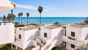 A coastal residential area with white buildings, palm trees, and a clear view of the sea. - APARTMENT TANSY DIRECTLY BY THE SEA WITH A DREAM SEA VIEW AND POOL (Armacao de Pera)