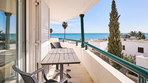 A balcony with a wooden table and chairs, overlooking a clear blue sea and palm trees. - APARTMENT TANSY DIRECTLY BY THE SEA WITH A DREAM SEA VIEW AND POOL (Armacao de Pera)