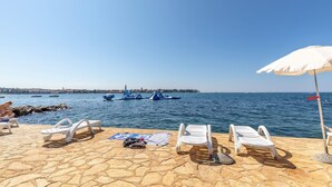 A beachside view with lounge chairs, a white umbrella, and boats on the water.
