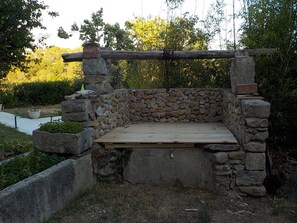 Ein Sitzbereich im Freien aus Stein mit einer hölzernen Bank und einer darüberliegenden Pergola.
