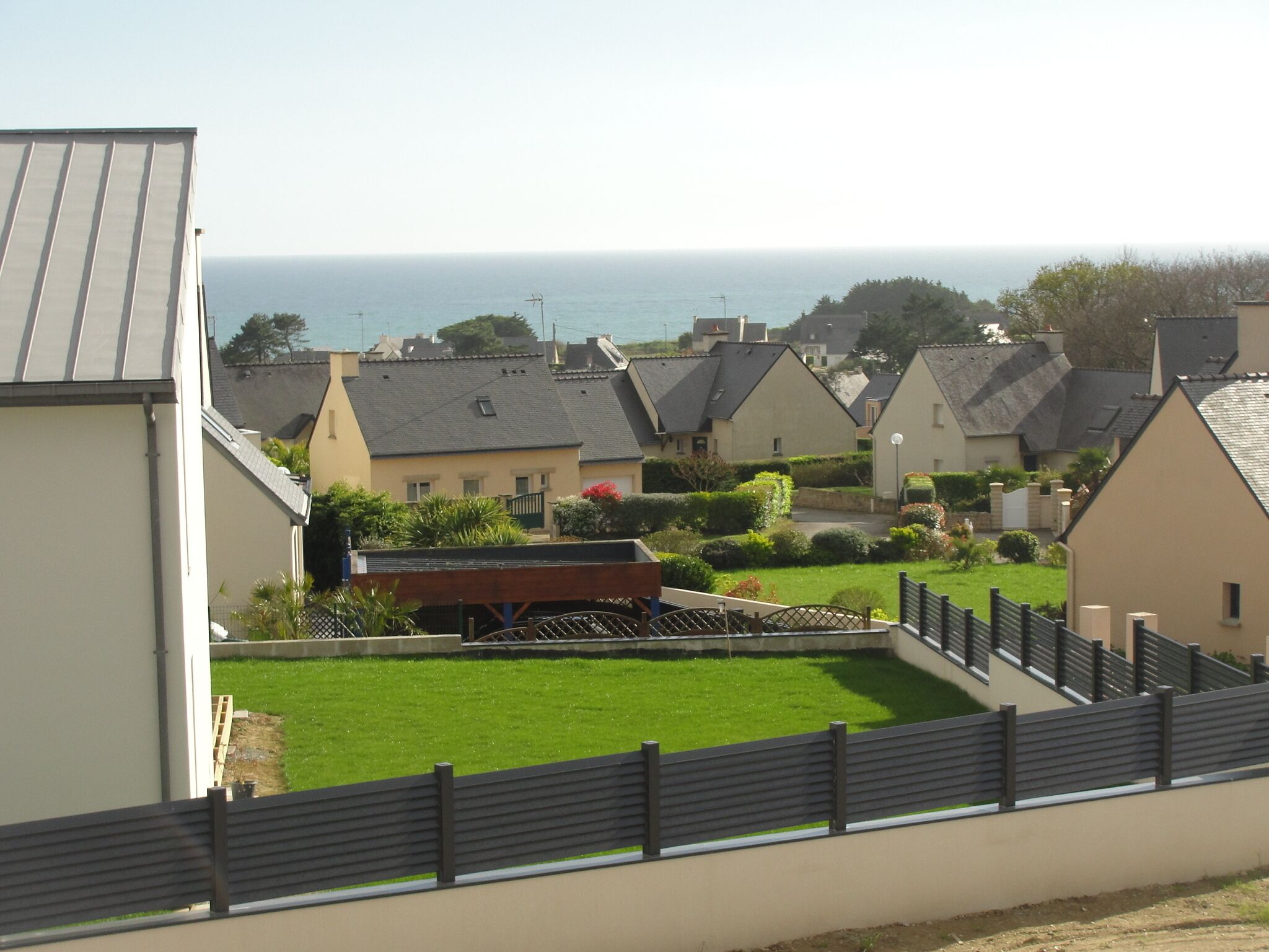 A residential area with houses, a grassy lawn, and a view of the sea.