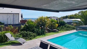A poolside area with a clear view of the sea, surrounded by lush greenery and modern outdoor furniture.
